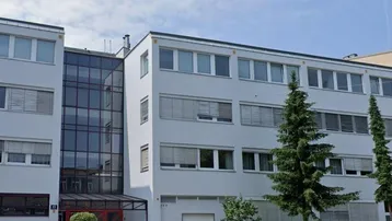 Modernes Bürogebäude mit heller Fassade und großer Glasfront am Eingangsbereich.