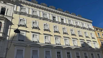 Fassade eines historischen Gebäudes mit vielen Fenstern und Jalousien unter blauem Himmel.