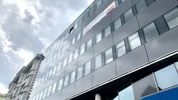 Moderne Bürogebäude-Fassade mit großen Fenstern und einem 'zu vermieten'-Schild unter bewölktem Himmel.