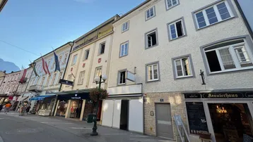 Historisches Gebäude an einer belebten Einkaufsstraße mit traditioneller Architektur und Geschäften im Erdgeschoss.