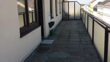 Langer Balkon mit Fliesenboden, Markise und Blick auf die umliegenden Dächer.