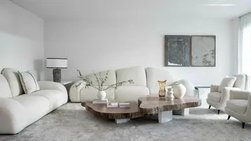 Helles, modernes Wohnzimmer mit bequemen, geschwungenen Sofas, einem einzigartigen Couchtisch aus Naturholz und stilvoller Dekoration.