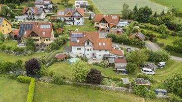Luftaufnahme einer Wohnsiedlung mit mehreren Häusern, umgeben von viel Grün und Feldern.