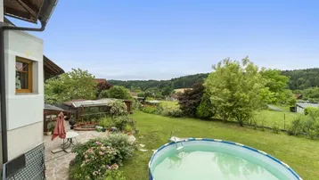 Panoramablick von einer erhöhten Terrasse auf den Garten mit Pool und die grüne Umgebung.