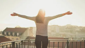 Frau genießt die Sonne auf einem Balkon mit weitem Blick über eine Stadt.