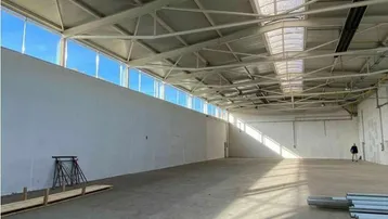 Große, leere Industriehalle mit hohen Decken, Betonboden und viel Tageslicht durch Fenster und Oberlichter.