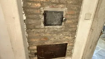 Detailansicht eines gemauerten Ofens mit Metalltüren im Kellerbereich, traditionelle Heizquelle.