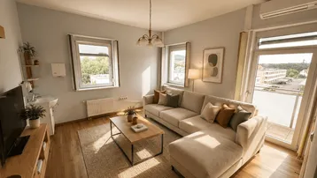 Helles Wohnzimmer mit beigem Ecksofa, Holzboden und Zugang zum Balkon, ausgestattet mit Klimaanlage.