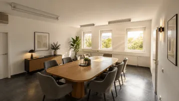 Geräumiger Konferenzraum mit modernem Holztisch, bequemen Stühlen und Blick ins Grüne durch große Fenster.