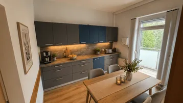 Moderne Küche mit Essbereich, Holzboden und Zugang zum Balkon, ausgestattet mit hochwertigen Geräten.
