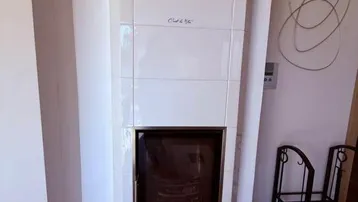 Traditioneller weißer Kachelofen als zentrale Wärmequelle im Wohnbereich mit Holzboden.