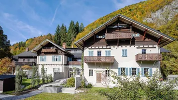 Traditionelles Gebäude mit Holzbalkonen und Bergblick, umgeben von herbstlicher Natur.