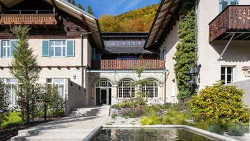 Eingangsbereich eines charmanten Gebäudes mit traditioneller Architektur, umgeben von grüner Landschaft und einem dekorativen Wasserbecken.