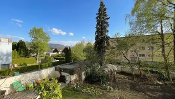 Blick auf den Garten mit kleinen Beeten, einem Schuppen und Bergsicht im Hintergrund.