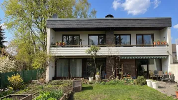 Rückansicht des Hauses mit gepflegtem Garten, Hochbeeten und einer möblierten Terrasse.