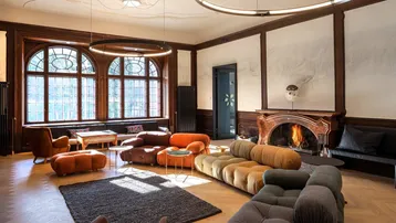 Großzügiges Wohnzimmer mit Kamin, hohen Bogenfenstern und modernen, farbigen Sitzmöbeln.