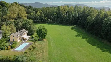 Luftaufnahme eines Landhauses mit Pool, umgeben von weitläufigen Grünflächen und Wäldern.