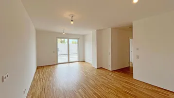 Heller Wohnbereich mit Parkettboden und Zugang zu einem Balkon oder einer Terrasse.