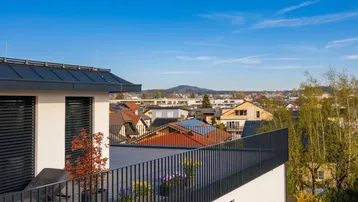 Geräumige Dachterrasse mit modernem Geländer und weitem Blick über die Stadt und die umliegende Landschaft.