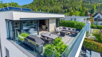 Geräumige Dachterrasse mit modernen Gartenmöbeln, Grillbereich und Blick auf die umliegende grüne Landschaft.