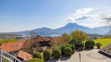 Panoramablick vom Balkon auf den See und die umliegende Berglandschaft unter blauem Himmel.