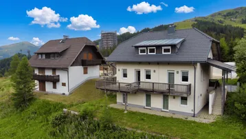 Zwei Wohnhäuser in alpiner Landschaft mit Blick auf die umliegenden Berge und Wälder.