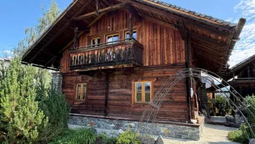 Traditionelles Holzchalet mit geschnitztem Balkon und gepflegtem Vorgarten unter blauem Himmel.