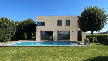 Modernes Haus mit klaren Linien, großem Garten und privatem Swimmingpool unter blauem Himmel.
