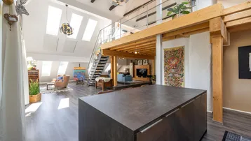 Großzügiger offener Wohnbereich mit Kücheninsel, hohen Decken, sichtbaren Holzbalken und Galerie.
