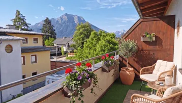 Sonniger Balkon mit Rattanmöbeln, Blumenkästen und herrlichem Bergblick in die Alpen.