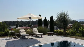 Großzügiger Außenbereich mit Pool, Liegestühlen und Sonnenschirm unter blauem Himmel.