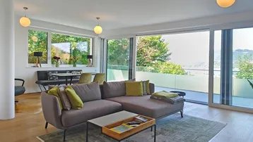 Helles Wohn- und Esszimmer mit modernem Sofa, Holzboden und großen Fenstern mit Zugang zur Terrasse und grüner Aussicht.