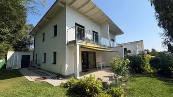 Modernes Haus mit gepflegtem Garten, Terrasse und Balkon unter strahlend blauem Himmel.