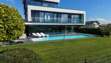 Moderne Villa mit weitläufigem Garten, großem Pool und Liegeflächen unter blauem Himmel.