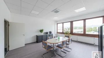 Konferenzraum mit großem Tisch, Stühlen, Schränken und Fenstern mit Ausblick auf die Umgebung.