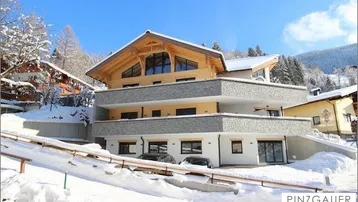 Modernes Gebäude in alpiner Winterlandschaft mit schneebedeckten Dächern und Balkonen unter blauem Himmel.