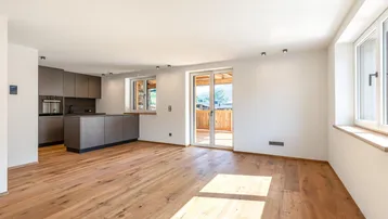 Heller, offener Wohnbereich mit moderner grauer Küche, Holzboden und Zugang zu einem Balkon.