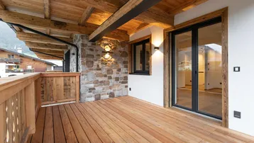 Geräumiger Balkon mit Holzboden, Steinwand und Holzbalkendecke, ideal für entspannte Stunden im Freien.