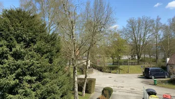 Blick von oben auf Bäume, einen Parkplatz und die Umgebung an einem sonnigen Tag.