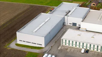 Luftaufnahme eines modernen Industriegebäudes mit Flachdach und angrenzenden Feldern unter klarem Himmel.