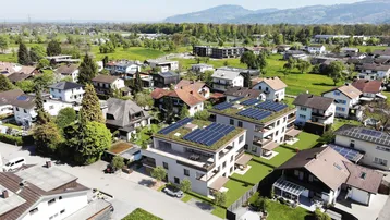 Luftaufnahme der modernen Mehrfamilienhäuser mit Photovoltaikanlage auf dem Dach und Bergblick.