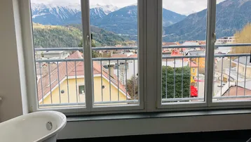 Freistehende Badewanne mit Panoramablick auf die Berge und die Stadt durch große Fenster.