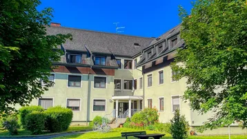Mehrfamilienhaus mit gepflegter Grünanlage und Sitzgelegenheiten im Freien unter blauem Himmel.