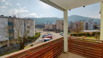 Geräumiger Balkon mit Holzboden und Blick auf die Umgebung, Berge und den Parkplatz.