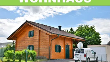Blockhaus mit Satteldach und grünen Fensterläden, umgeben von einem gepflegten Garten.