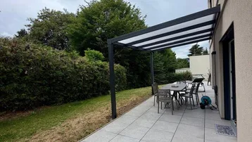 Große, modern geflieste Terrasse mit Pergola, Gartenmöbeln und angrenzendem Grünbereich.