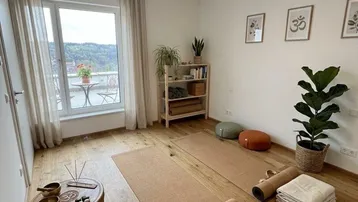 Heller Raum mit Holzboden, Yogamatten und Zugang zu einem französischen Balkon mit Aussicht.
