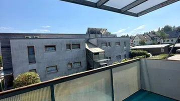 Überdachter Balkon mit Blick auf die umliegenden Gebäude und Grünflächen.