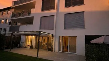 Moderne Wohnanlage mit gepflegtem Garten und überdachter Terrasse bei Sonnenuntergang.
