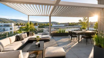 Geräumige Dachterrasse mit moderner Lounge-Möblierung, Essbereich und weitem Blick über die Stadt bei Sonnenuntergang.